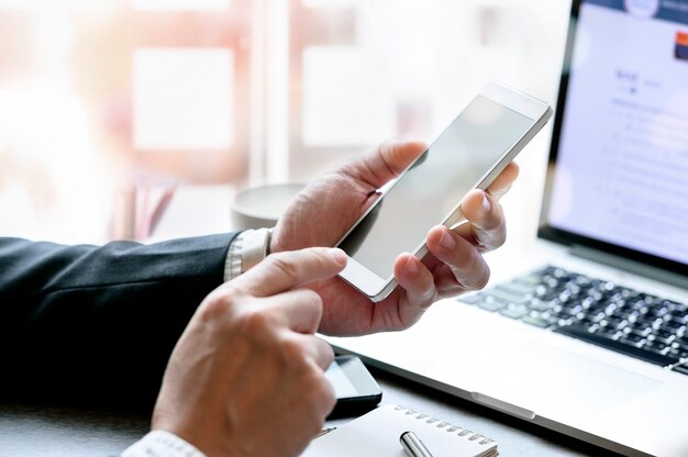 Cropped view of businessman hand using mobile smartphone while sitting at office desk.