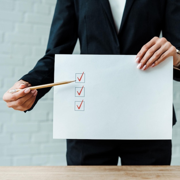 Photo cropped view of businesswoman holding pencil near paper with check list