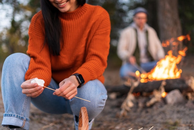 Vista ritagliata della donna caucasica che si gode la ricreazione all'aperto mentre tiene i marshmallow ai bastoncini e la prepara arrostita sul fuoco con il suo ragazzo. foto d'archivio