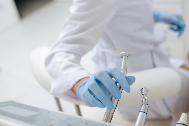 Cropped view of dentist taking stainless dental instrument