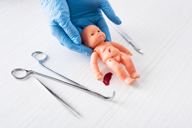 Cropped view of doctor in blue latex gloves holding baby doll with blood near medical instruments