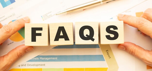 Cropped view of hands holding wooden cubes with FAQS lettering on work table.