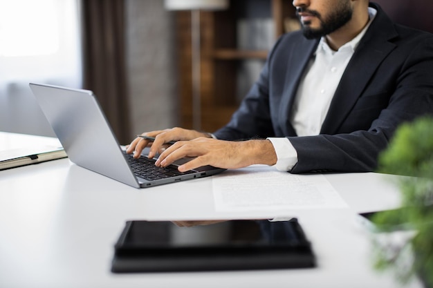 Cropped view of hands of young bearded businessman typing on laptop during work in office