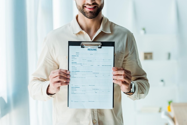 Cropped view of happy bearded man holding clipboard with resume letters