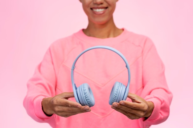 ピンクの背景に分離されたヘッドフォンを保持している幸せな女性のビューをトリミング