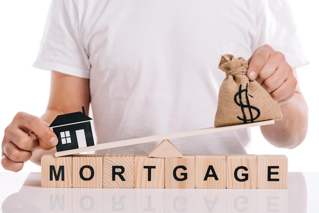 Cropped view of man holding moneybag and paper house on scales on cubes with mortgage lettering