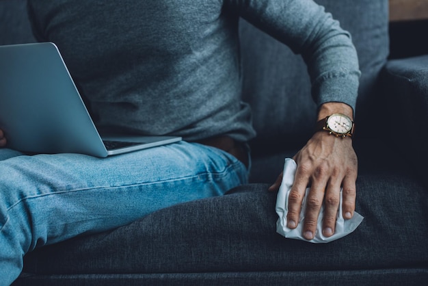 Cropped view of man holding napkin while watching pornography on laptop on couch