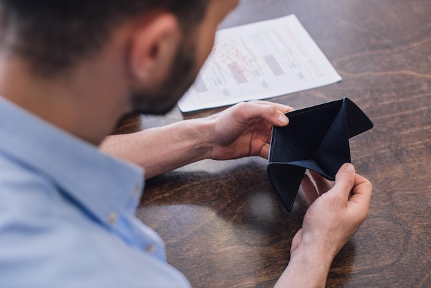 Cropped view of man looking at empty purse at table