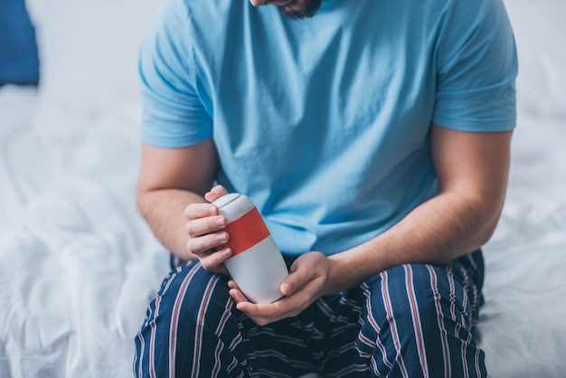 Photo cropped view of man sitting on bed and holding funeral urn