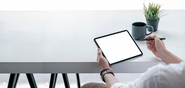 Cropped view of man using blank screen tablet sitting at white wooden table banner panoramic view