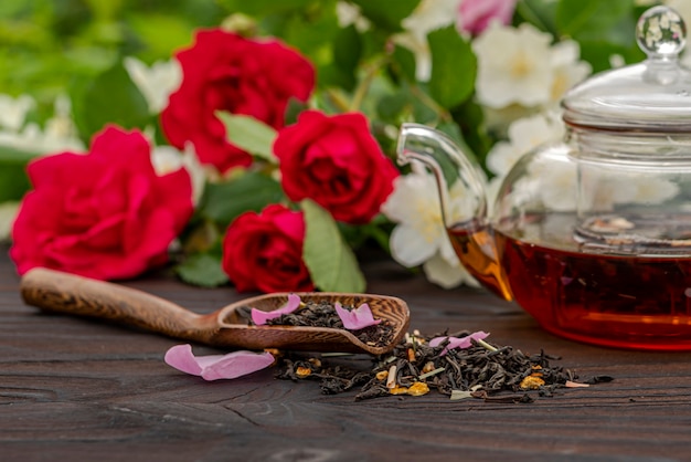 Фото Обрезанный вид бамбуковой ложки с чаем среди цветущих кустов роз и жасмина