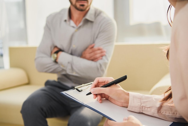 Cropped view of patient and psychologist writing diagnosis in clipboard in office