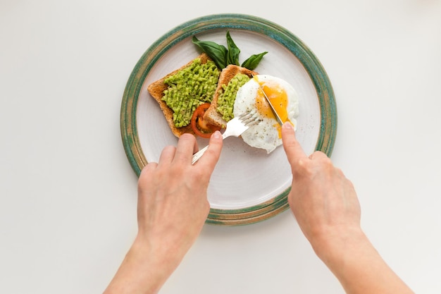 Cropped view of person eating fried egg and mashed avocado on toasts for breakfast isolated on