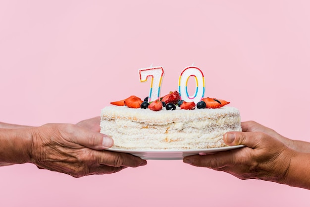 Cropped view of retired couple holding tasty birthday cake isolated on pink