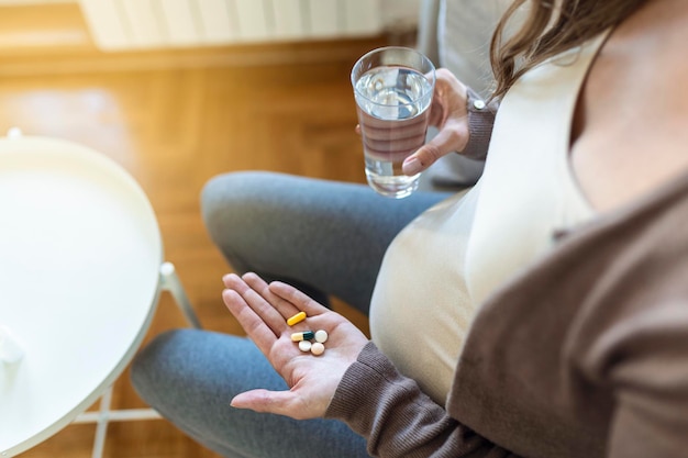 Cropped view of sick and ill pregnant woman holding different pills on palm hand, showing medical preparat on camera