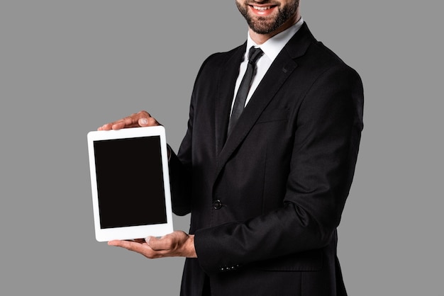 Photo cropped view of smiling businessman in black suit showing digital tablet with blank screen isolated