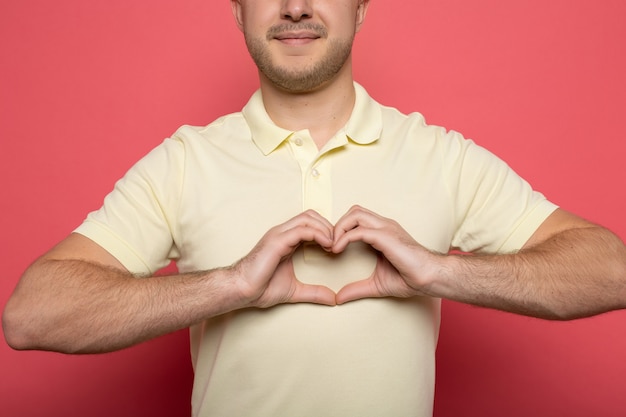 Cropped view of smiling man showing heart gesture on pink
