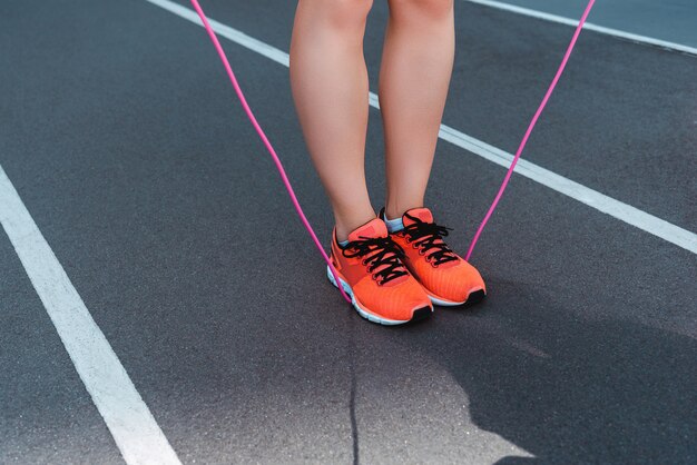 Foto vista ritagliata di sportiva in scarpe da ginnastica che tiene la corda per saltare sulla pista da corsa