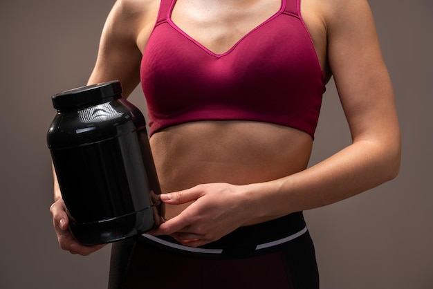 Cropped view of sporty beautiful woman in sportswear holding shaker with healthy protein drink isolated over brown studio background