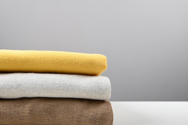 Cropped view of stack of folded colorful clothes on gray surface side view space for text Brown grey and yellow color tone High quality photo