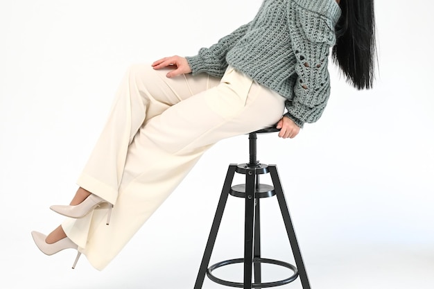 Cropped view of stylish woman in white trousers sits on a wooden black chair on white background