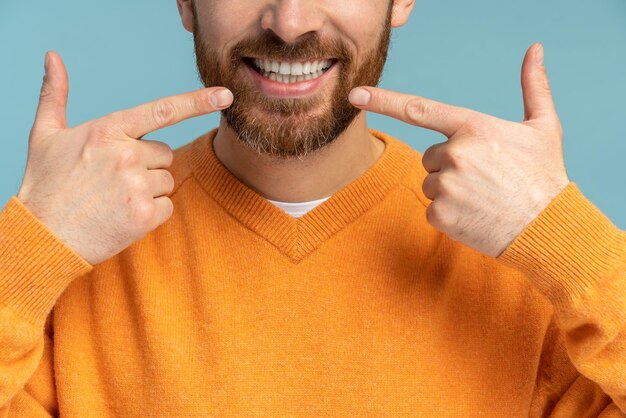 Cropped view of the successful positive bearded man pointing with fingers at camera with toothy smile Indoor studio shot isolated on blue background