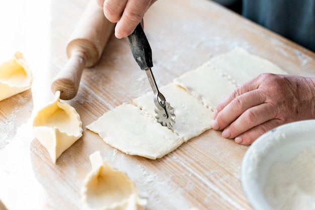 Cropped view of the unrecognisable woman cutting dough with special equipment at the wooden table with flour Stock photo