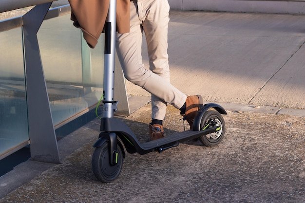 Cropped view of unrecognizable man leaning with his electric scooter for commuteing to work as an ecological alternative