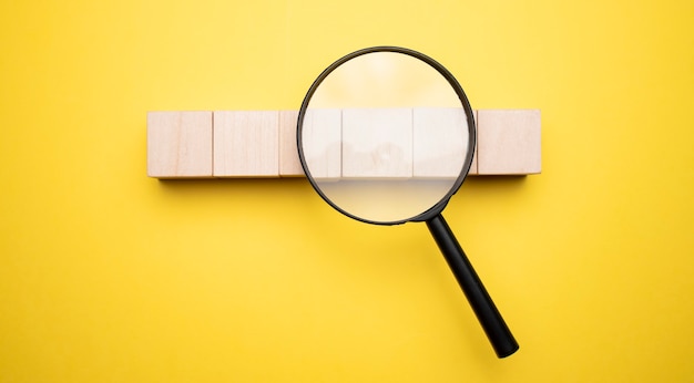 Cropped view of woman holding magnifying glass under wooden cubes with logo on yellow background