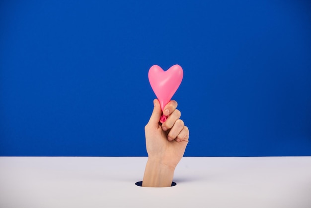 Cropped view of woman holding pink heartshaped balloon isolated on blue