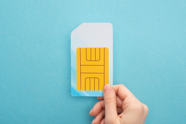 Cropped view of woman holding sim card on blue background