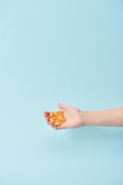 Photo cropped view of woman holding slices of tasty peeled tangerine in hand isolated on blue