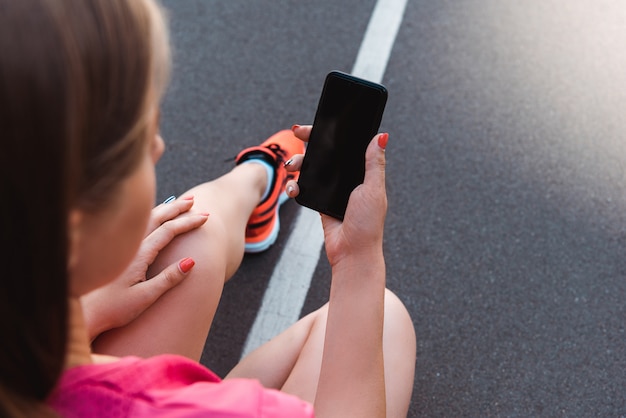 cropped view of woman holding smartphone with blank screen on running track