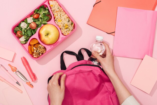 Cropped view of woman packing backpack near lunch box and stationery