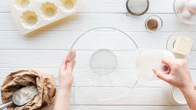 Cropped view of woman pouring sugar in bowl while cooking on table