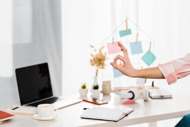 Cropped view of woman showing okay sign at workplace