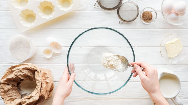 Cropped view of woman with scoop putting flour in bowl while cooking on table