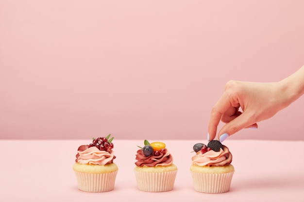 Cropped view of woman with sweet cupcakes with fruits and berries isolated on pink