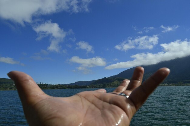 Photo cropped wet hand by lake against blue sky