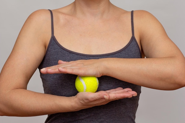 Foto corpo di donna tagliato che rotola una palla da tennis tra le mani facendo esercizi su uno sfondo grigio