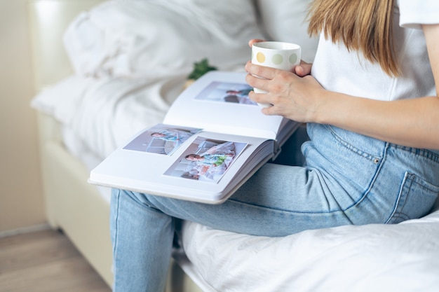 Foto mani tagliate della donna che tengono il caffè e guardano un album di foto di famiglia.