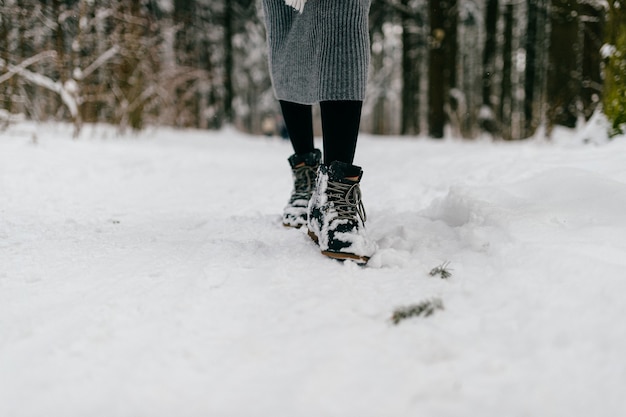 Gambe di donna ritagliate con gli stivali che camminano nella foresta di neve