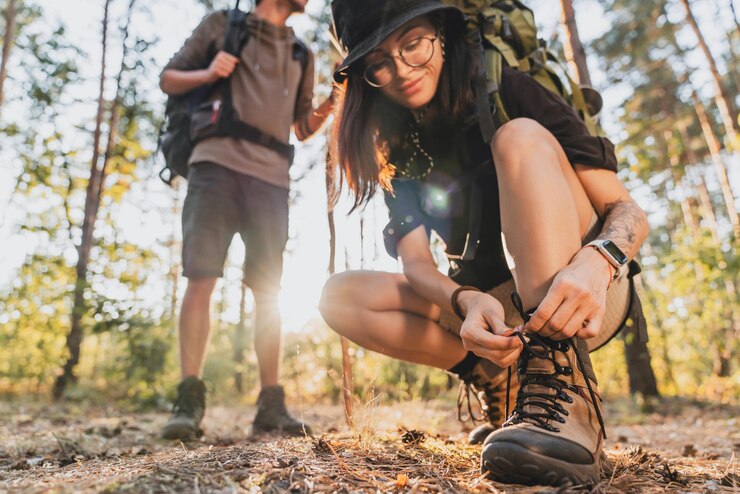 Photo cropped of woman tying hiking boot outdoors on trail in forest while travel with her boyfriend