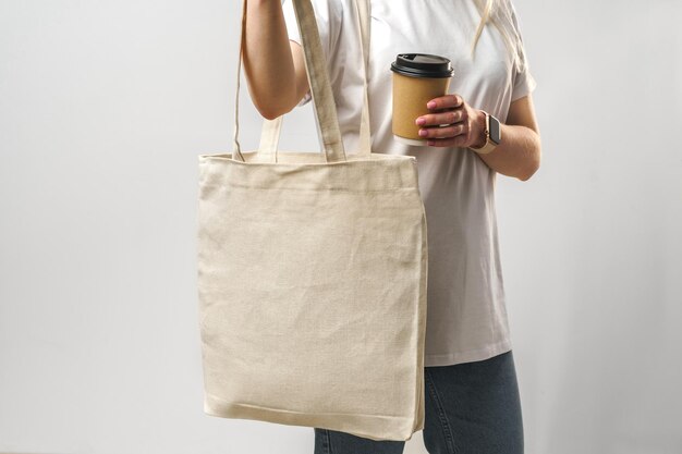 Cropped woman with cotton bag and paper coffee cup studio shot