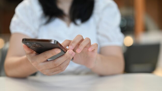 Cropped Young Asian woman using her smartphone at her desk chatting scrolling on social media