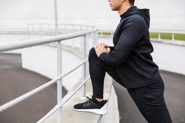 Cropped a young confident sportsman exercising at the stadium outdoors, stretching