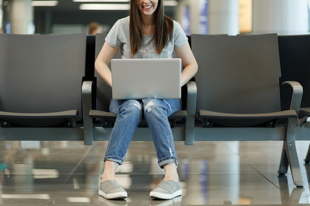 국제 공항의 로비 홀에서 기다리는 동안 노트북에서 작업하는 자른 젊은 즐거운 여행자 관광 여자