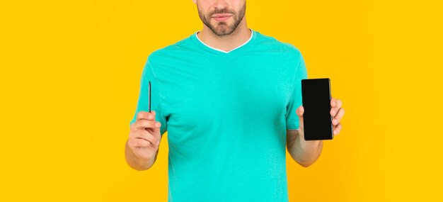 Cropped young man presenting phone and stylus on yellow background, presentation