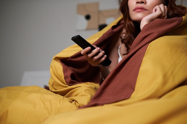 Cropped young woman wrapped in thick blanket and watching tv show