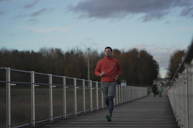 Foto cross country joggen op het platteland man in oranje sweatshirt loopt over houten brug in natie